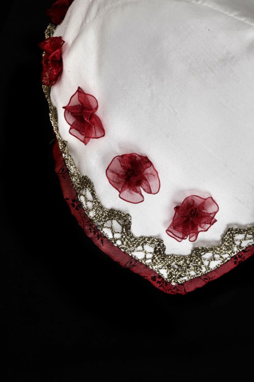 Vit hätta i siden kantad med med rött siden och guldspets, dekorerad med handsydda chiffongblommor. (Foto Lasse Modin)