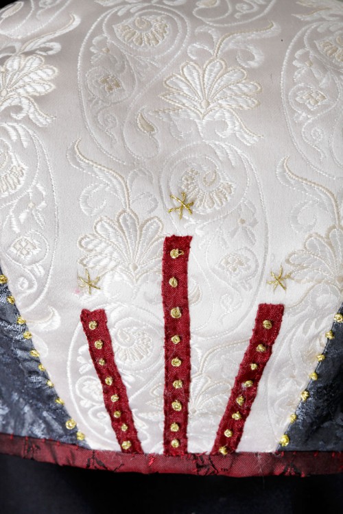 Grå och vit hätta i siden kantad med med rött siden, dekorerad med stjärnor och franska knutar i guldtråd. (Foto Lasse Modin)